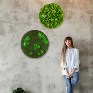 žena stojaca pri stene so zelenými hodinami na jej strane a rastlinou na druhej strane, environmentálne umenie , machovy obraz, stabilizovany mach, machová stena, machová dekorácia